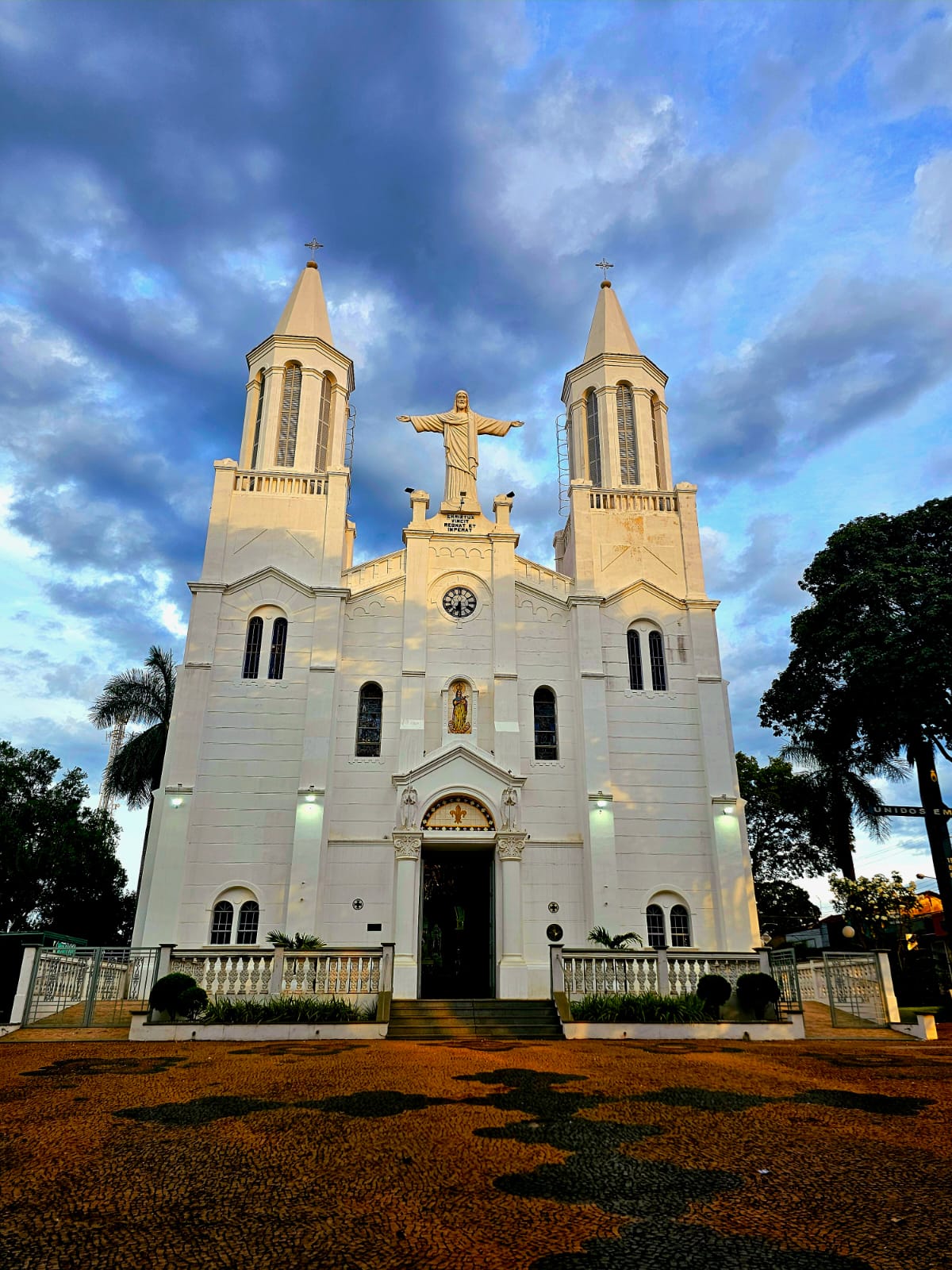 Fachada da Igreja Matriz da Paróquia Nossa Senhora do Belém em Descalvado, mostrando arquitetura clássica com duas torres simétricas, Cristo Redentor no topo, e céu azul ao fundo